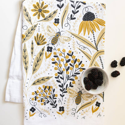 Floral and bee patterned towel with a bowl of blackberries on a white background