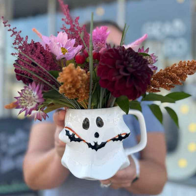 Ghost-shaped mug with flowers held by a person against a blurred background