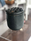 A black ceramic vase with a flower frog lid