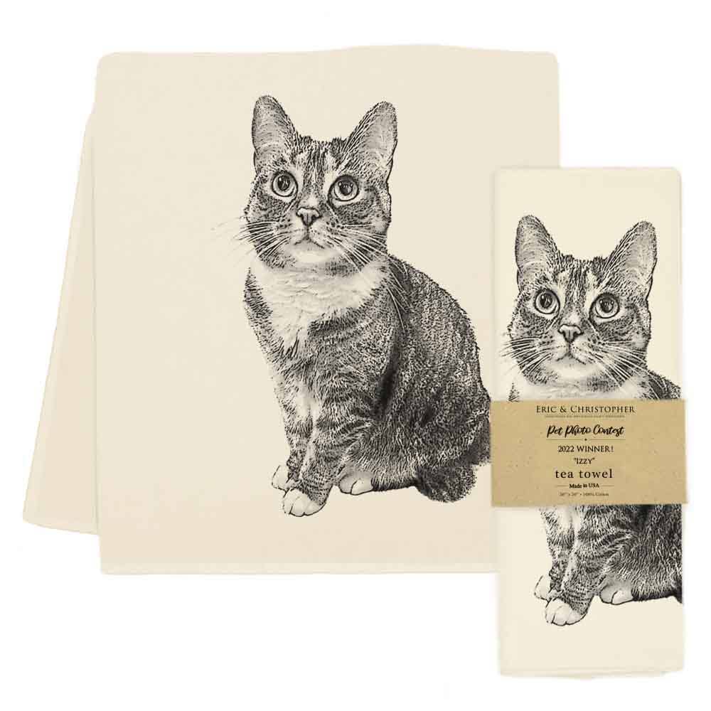 A cream-colored tea towel with a detailed black ink sketch of a tabby cat, shown alongside its matching paper packaging with a brown paper band.